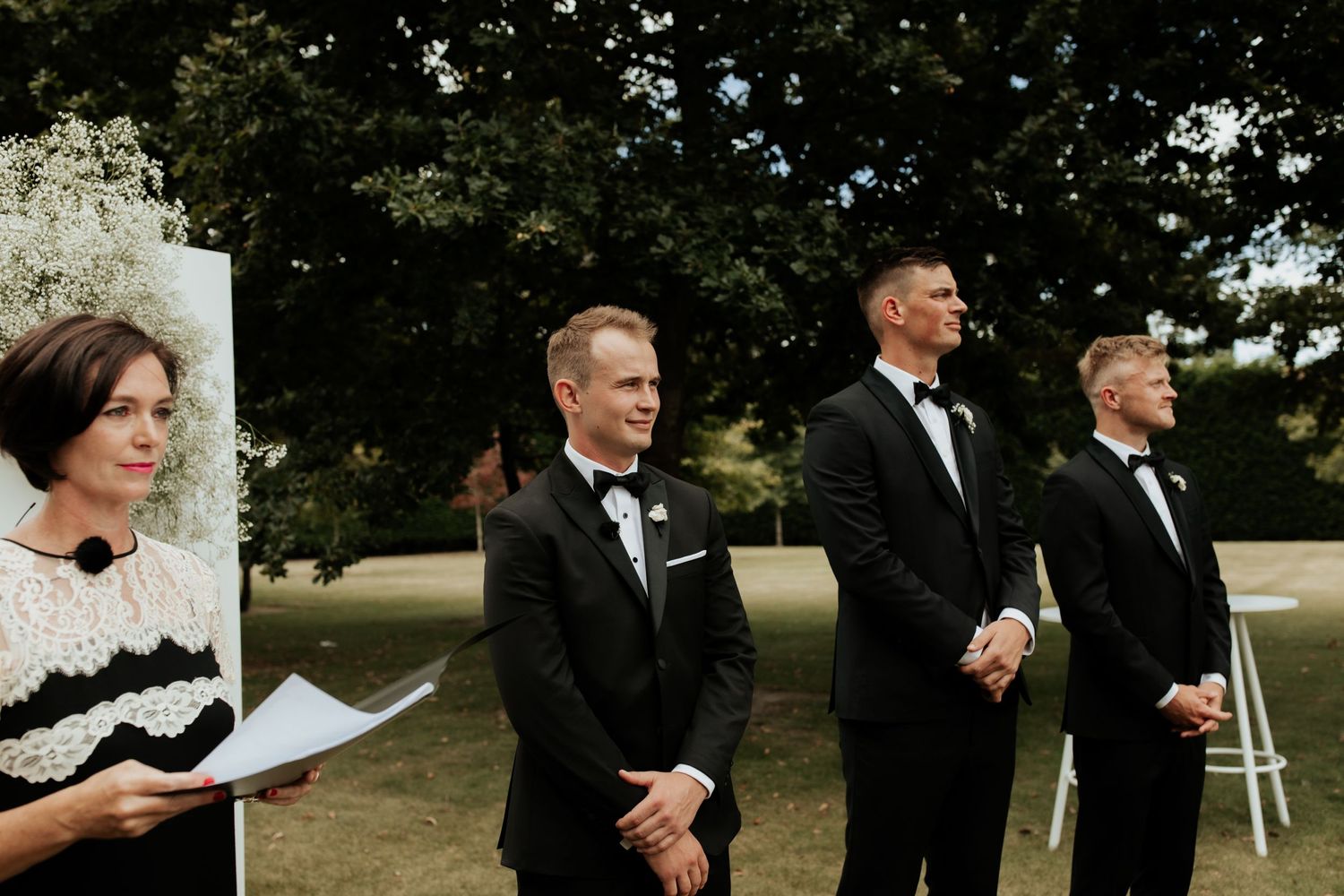 Wedding ceremony attendants standing in formal attire at outdoor venue.