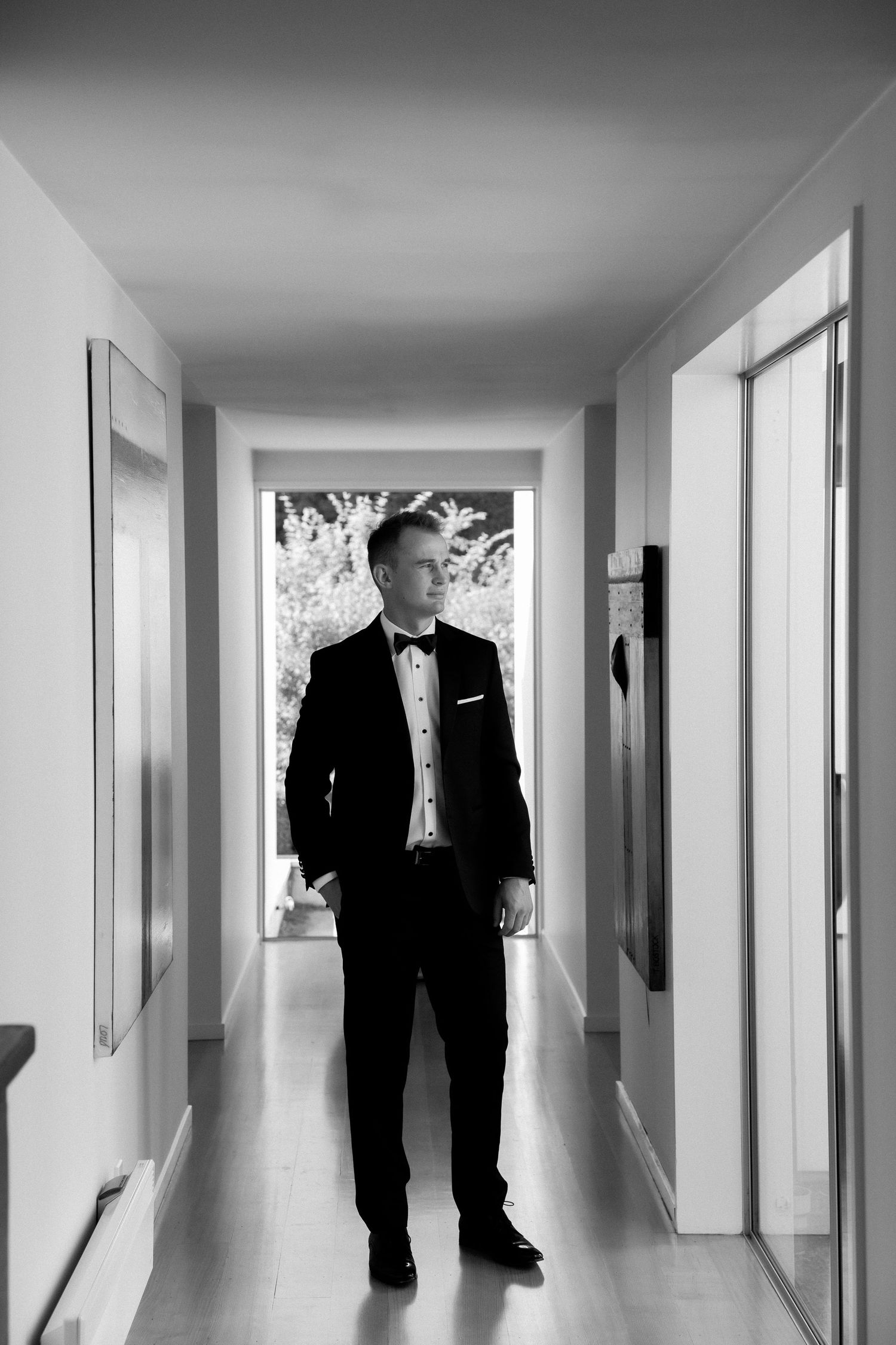 Classic black and white photo of person in tuxedo standing in modern white hallway.