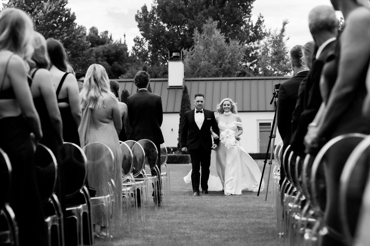 Black and white wedding ceremony photo with guests seated in rows outdoors.