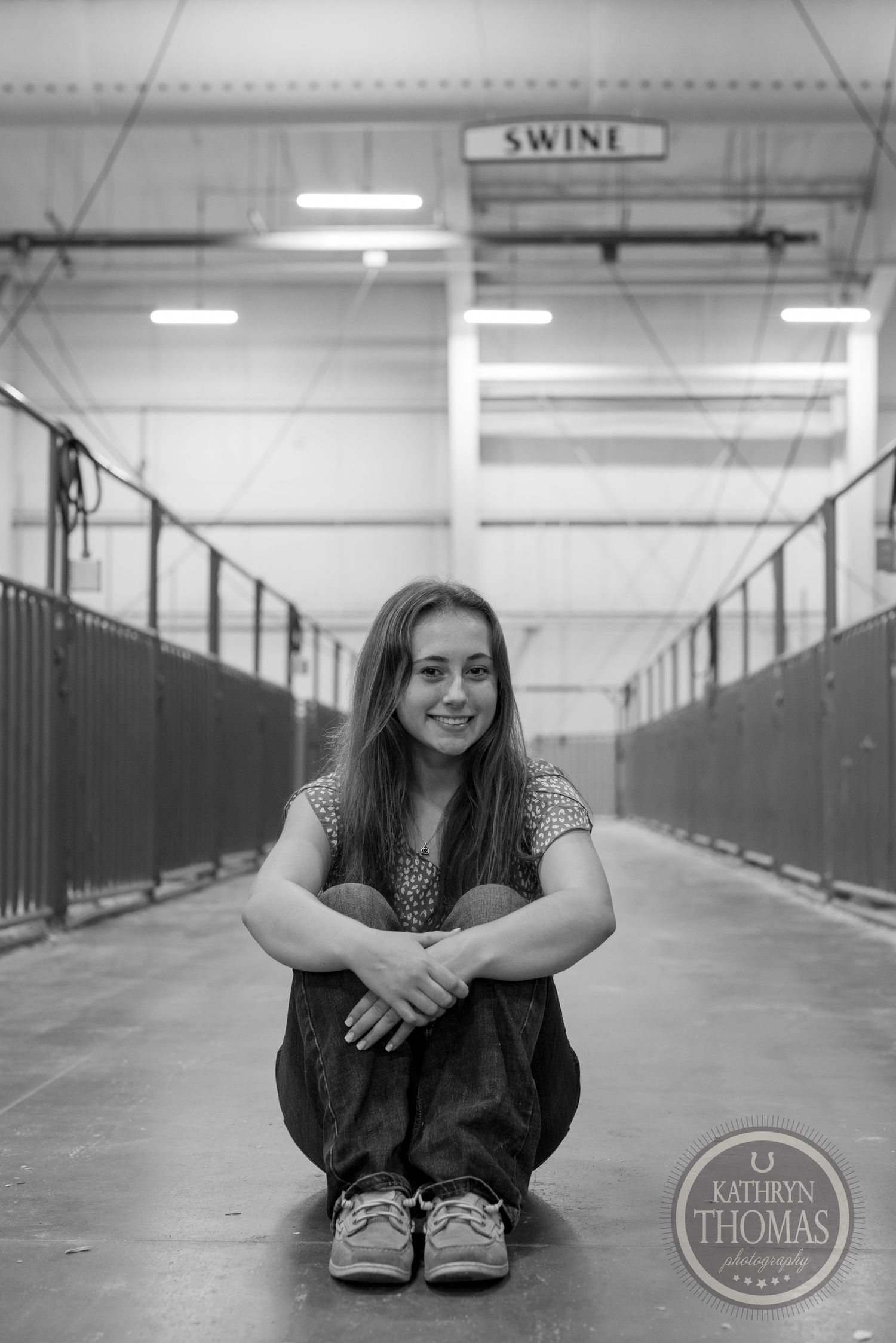 Black and white portrait under swine facility sign with metal stalls in background.