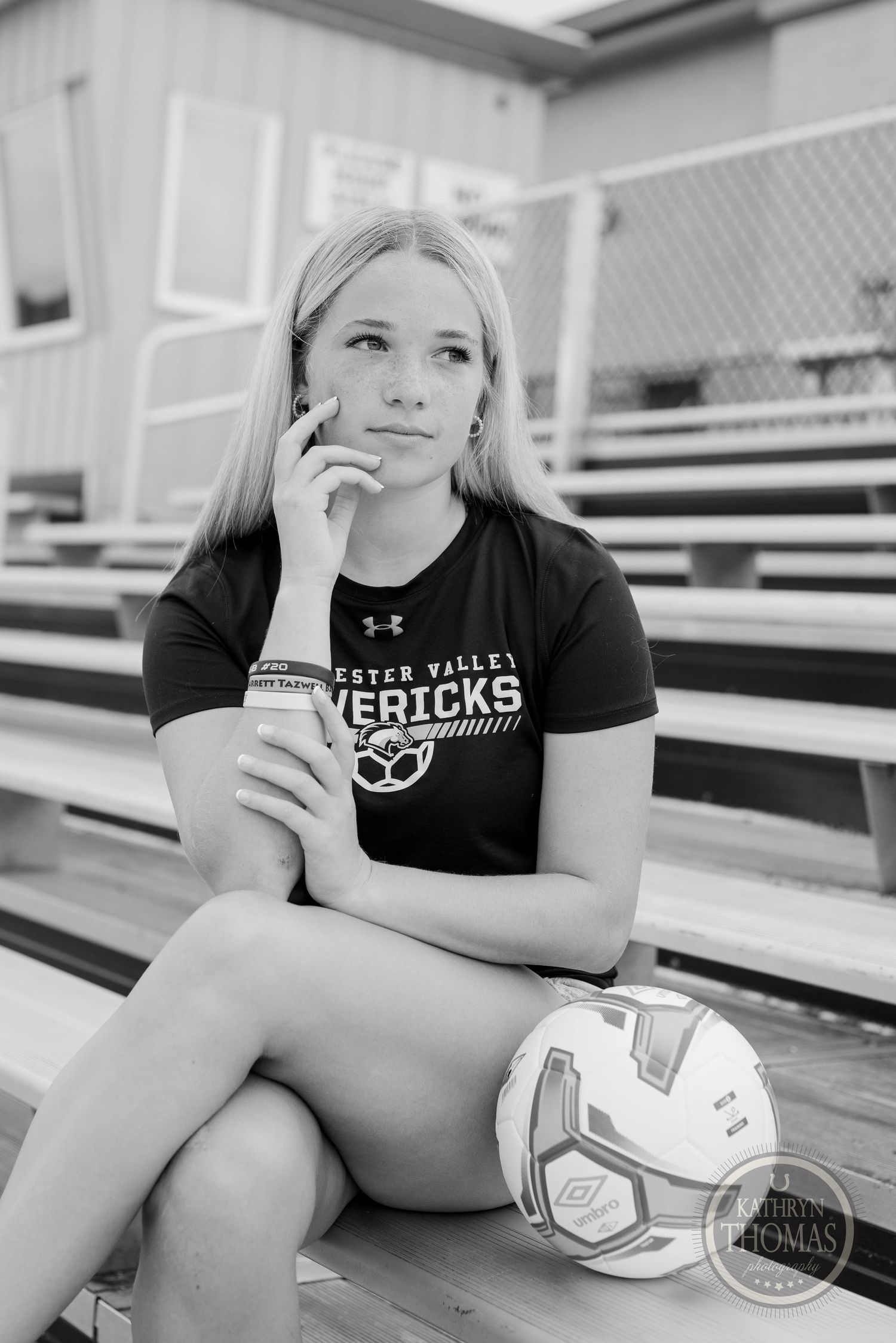 Black and white portrait of athlete with soccer ball sitting on bleachers in contemplative pose.