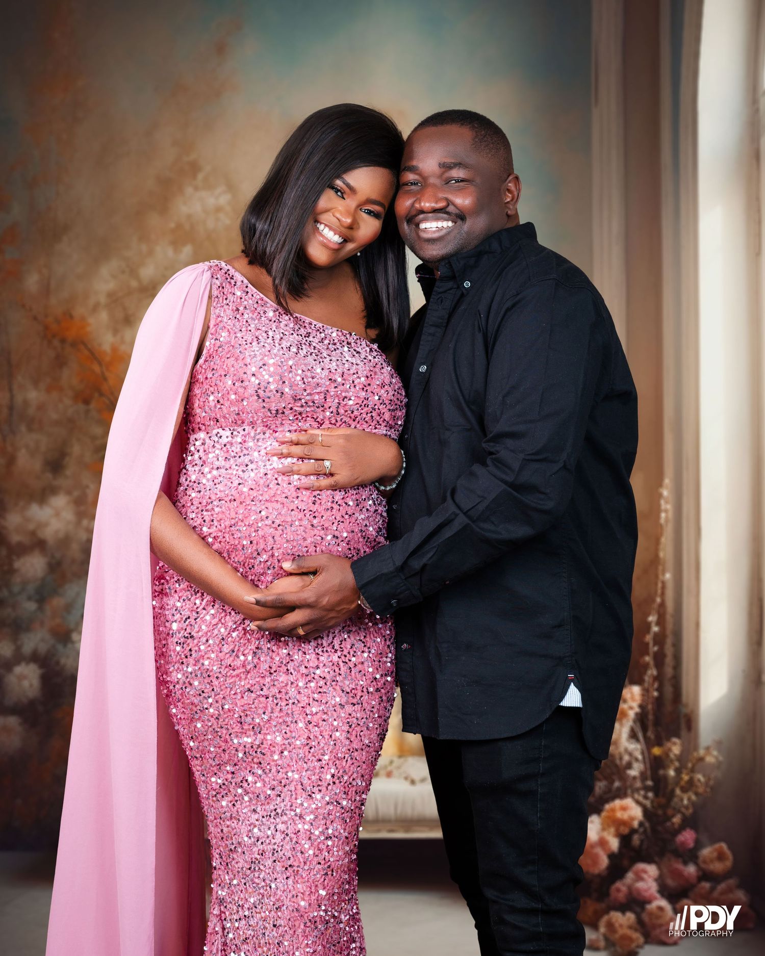 Expecting couple poses together, with mother wearing a sparkly pink gown for maternity photos.