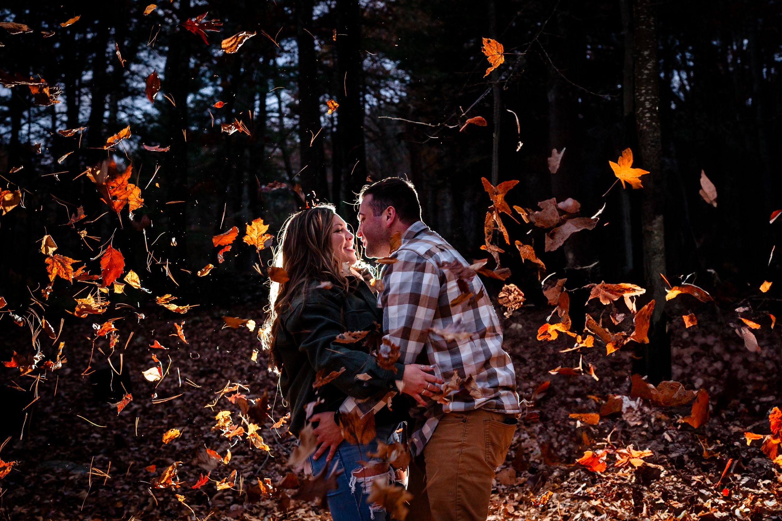 Person playfully jumping and tossing autumn leaves in a wooded area during fall.