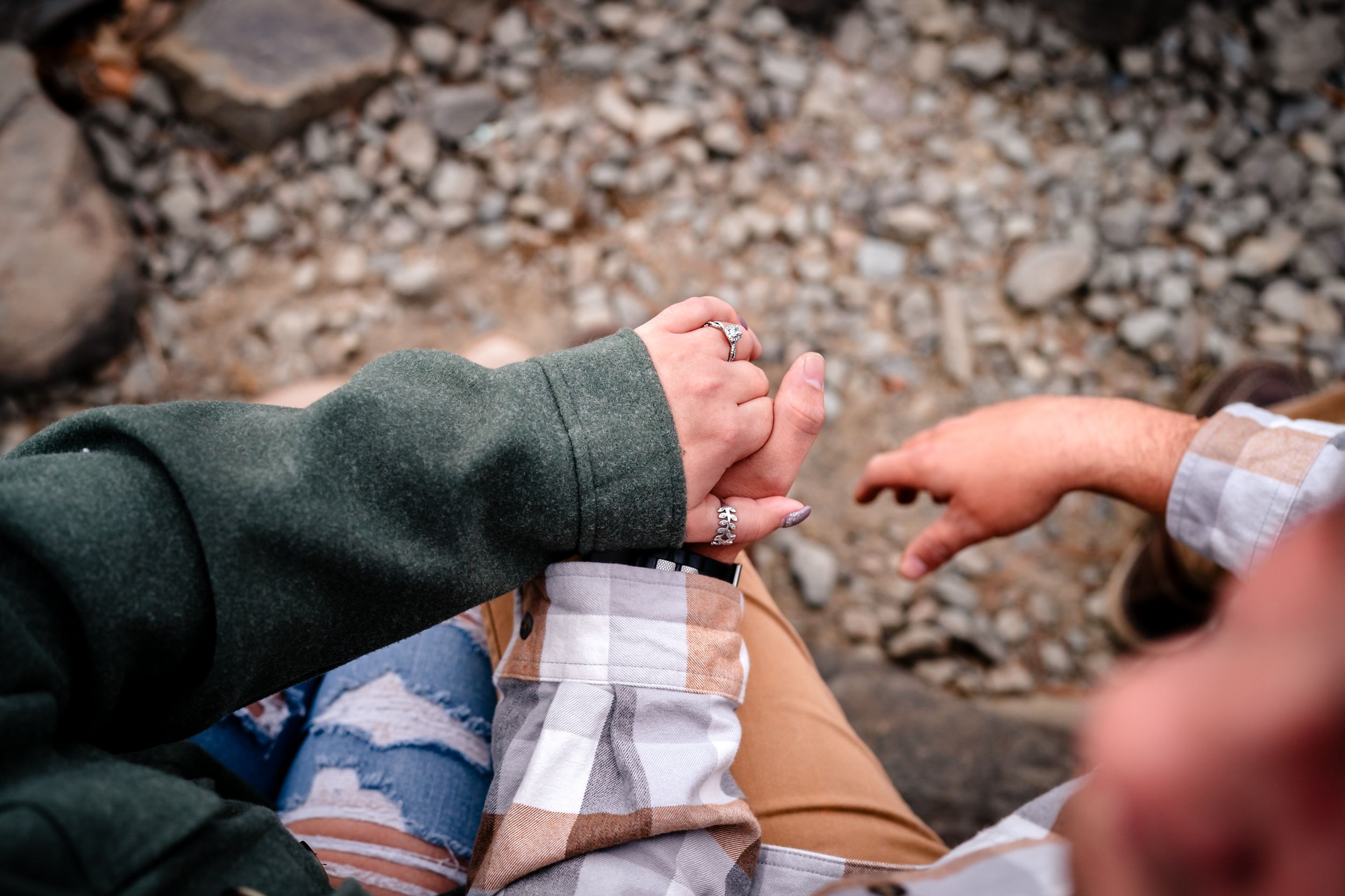 Close-up shots of hands holding engagement ring boxes by rocky shoreline.