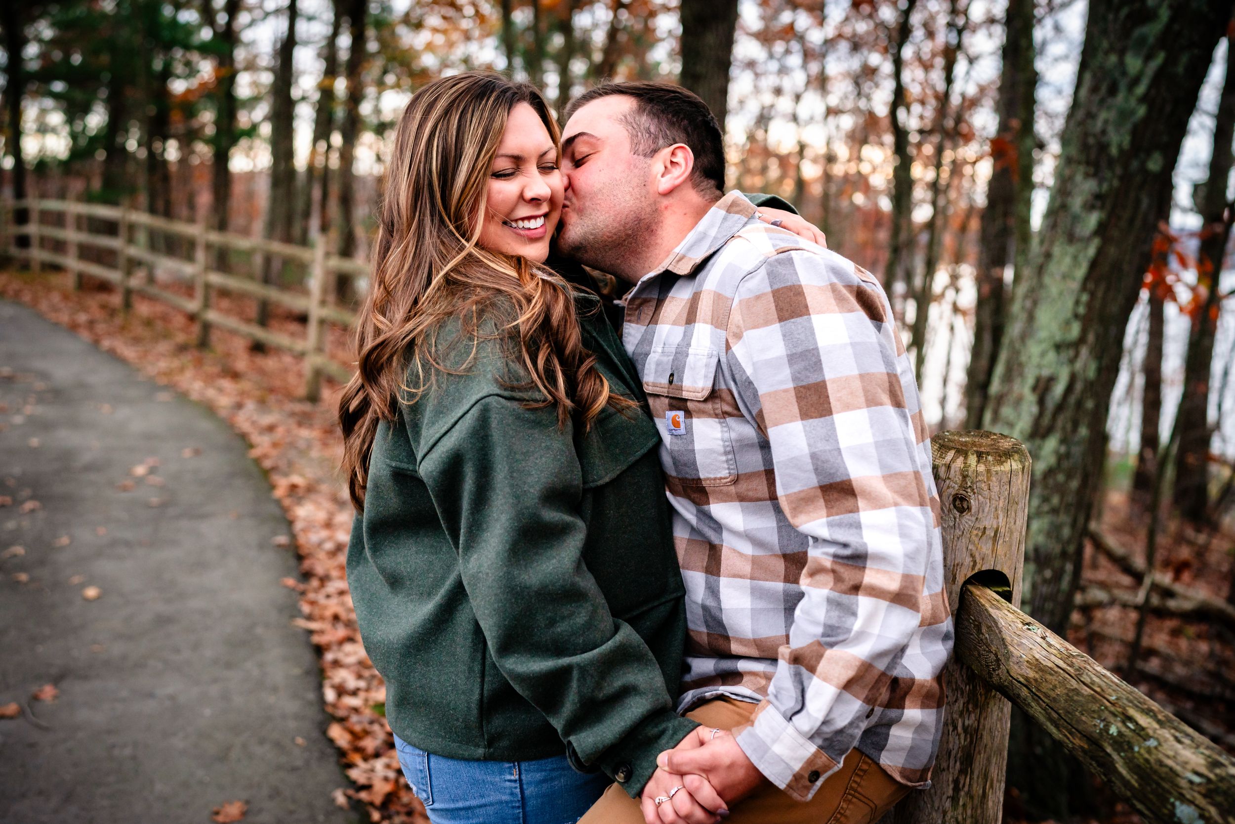 A couple shares a tender moment on a tree-lined path during autumn.