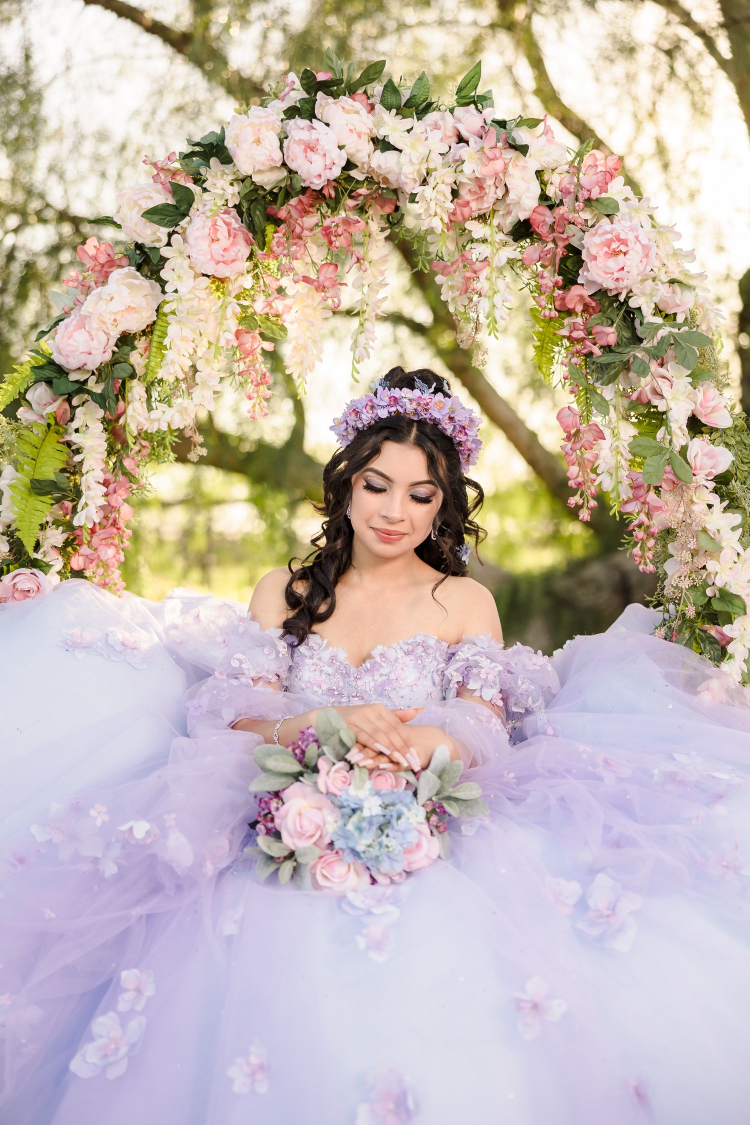 A lavender ballgown contrasts with a floral arch of pink roses and white blossoms in a dreamy garden setting.