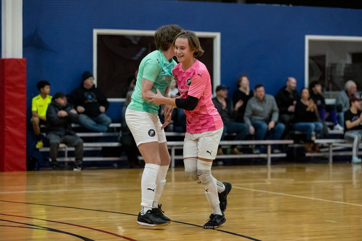 Players competing in indoor soccer match on blue court with red walls.