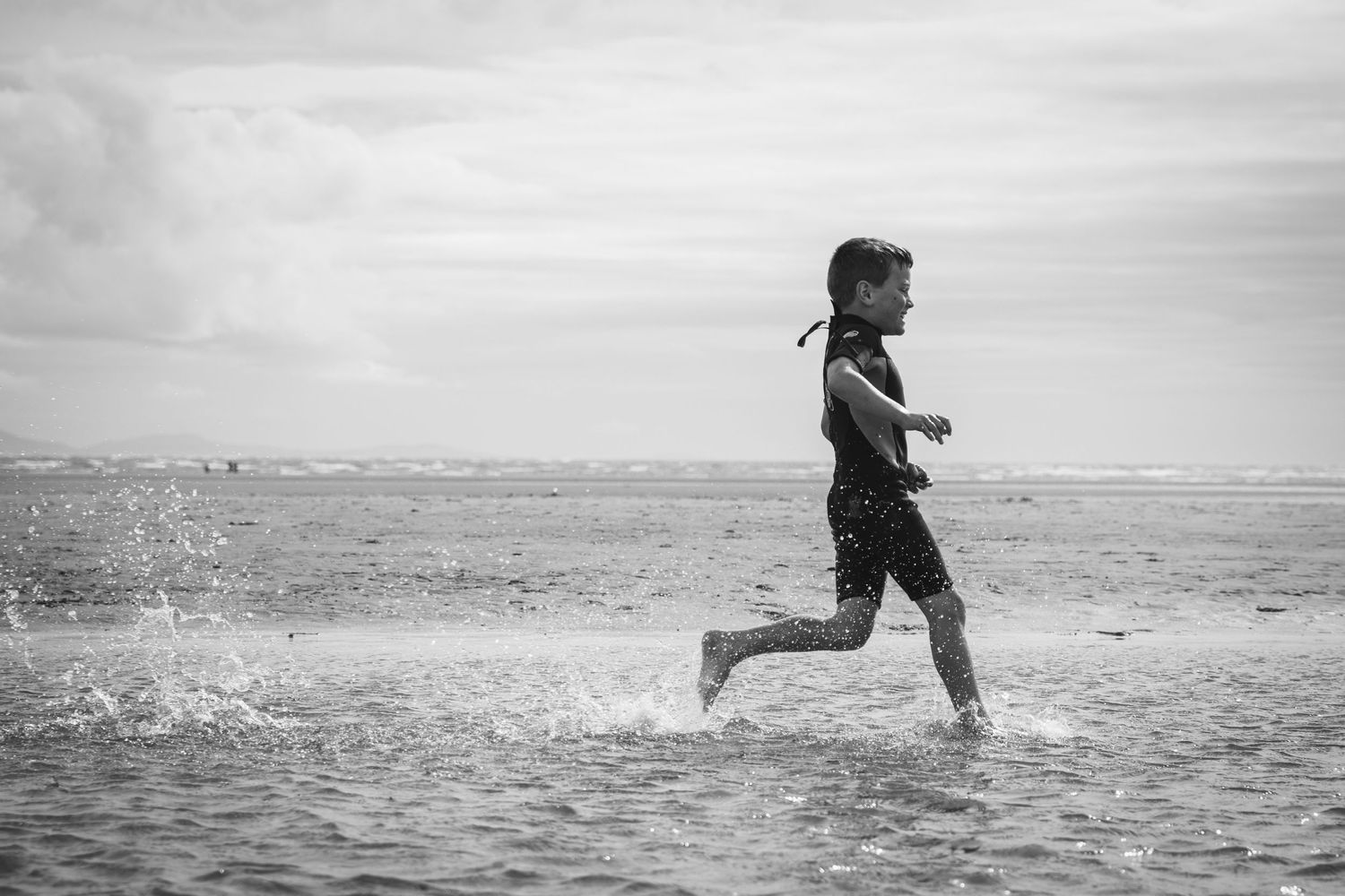 Black and white photo of someone running through shallow water at the beach.