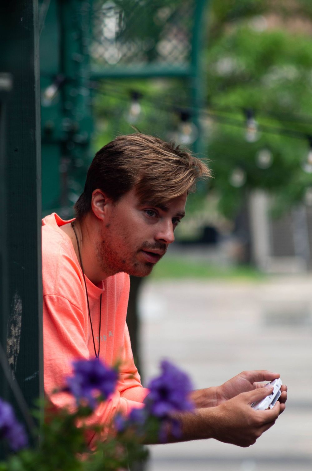 a man in a pink shirt leans over a railing holding a gameboy