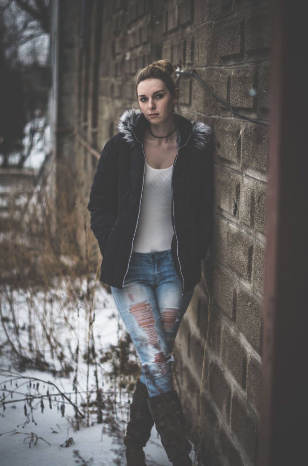 a woman leans against a stone wall in the winter.