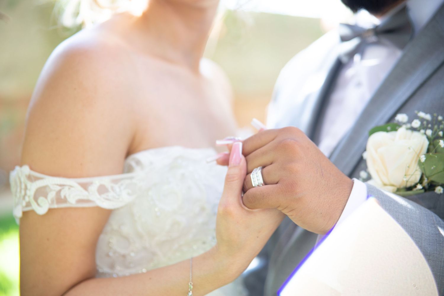 Close-up of newlyweds hands as groom adjusts bride's delicate lace sleeve during outdoor wedding ceremony.