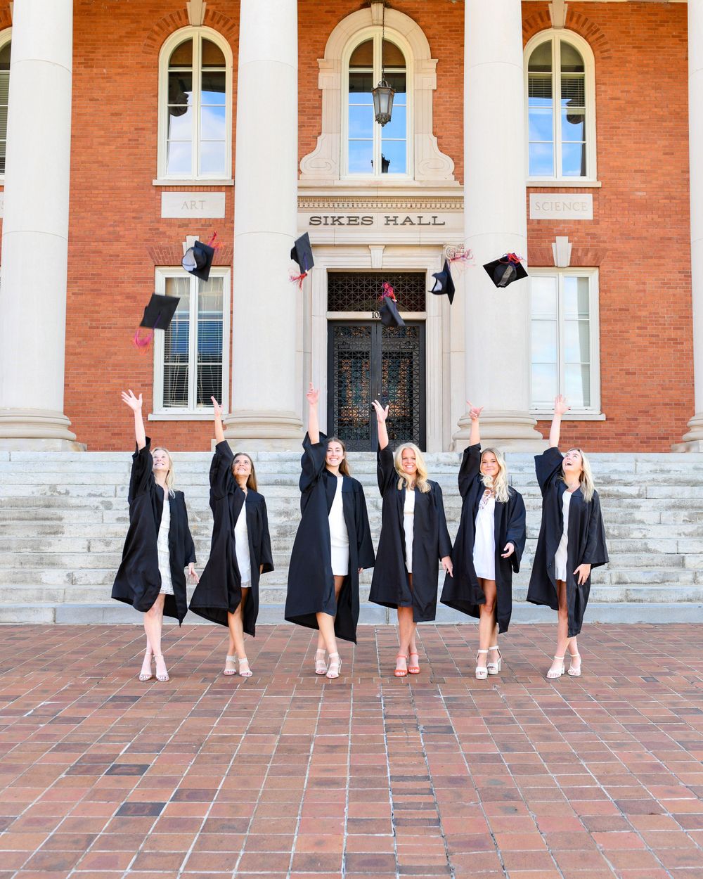 Graduates toss caps in celebration on brick steps of historic Sikes Hall.