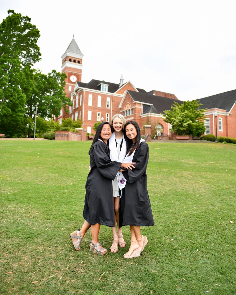 Graduation photo taken on a grassy lawn in front of a historic brick building with a distinctive clock tower.