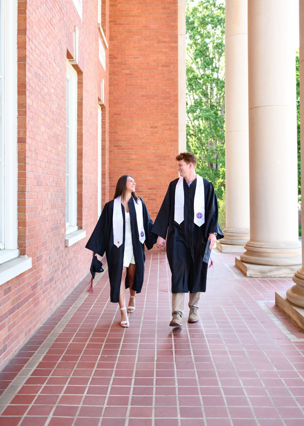 Graduates in caps and gowns walk together along covered brick walkway.