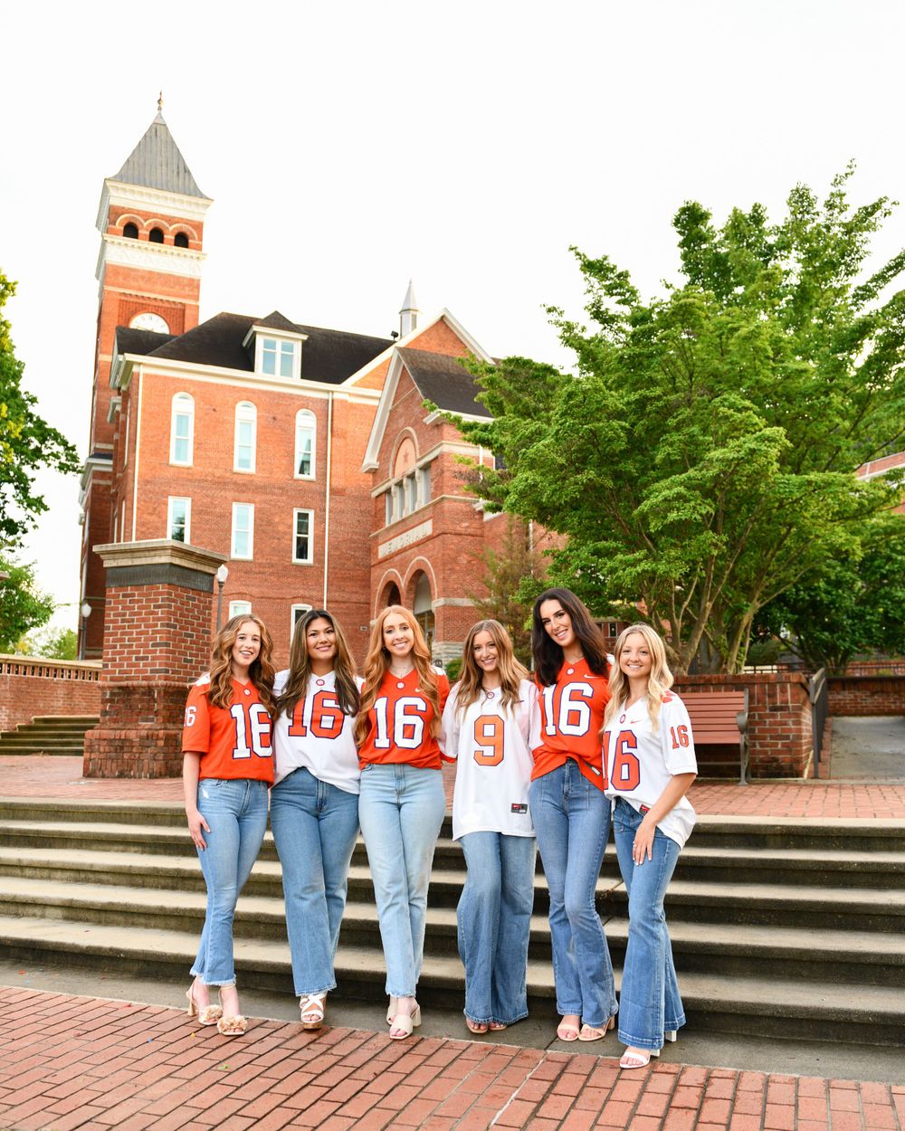 A group wearing matching orange jerseys with the number 16 poses on brick steps in front of a historic building.