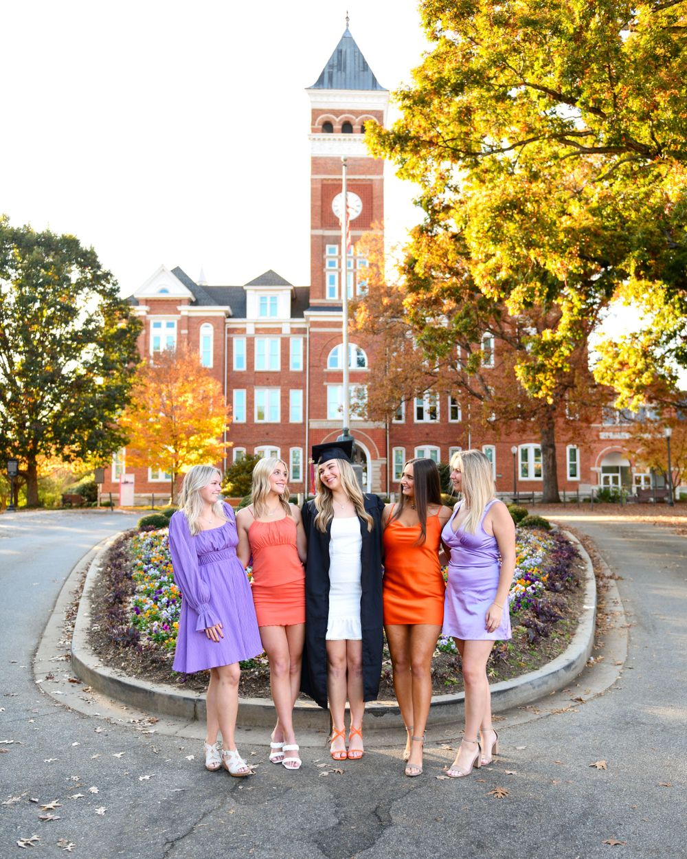Friends posing in colorful dresses in front of Clemson's iconic Tillman Hall during autumn.
