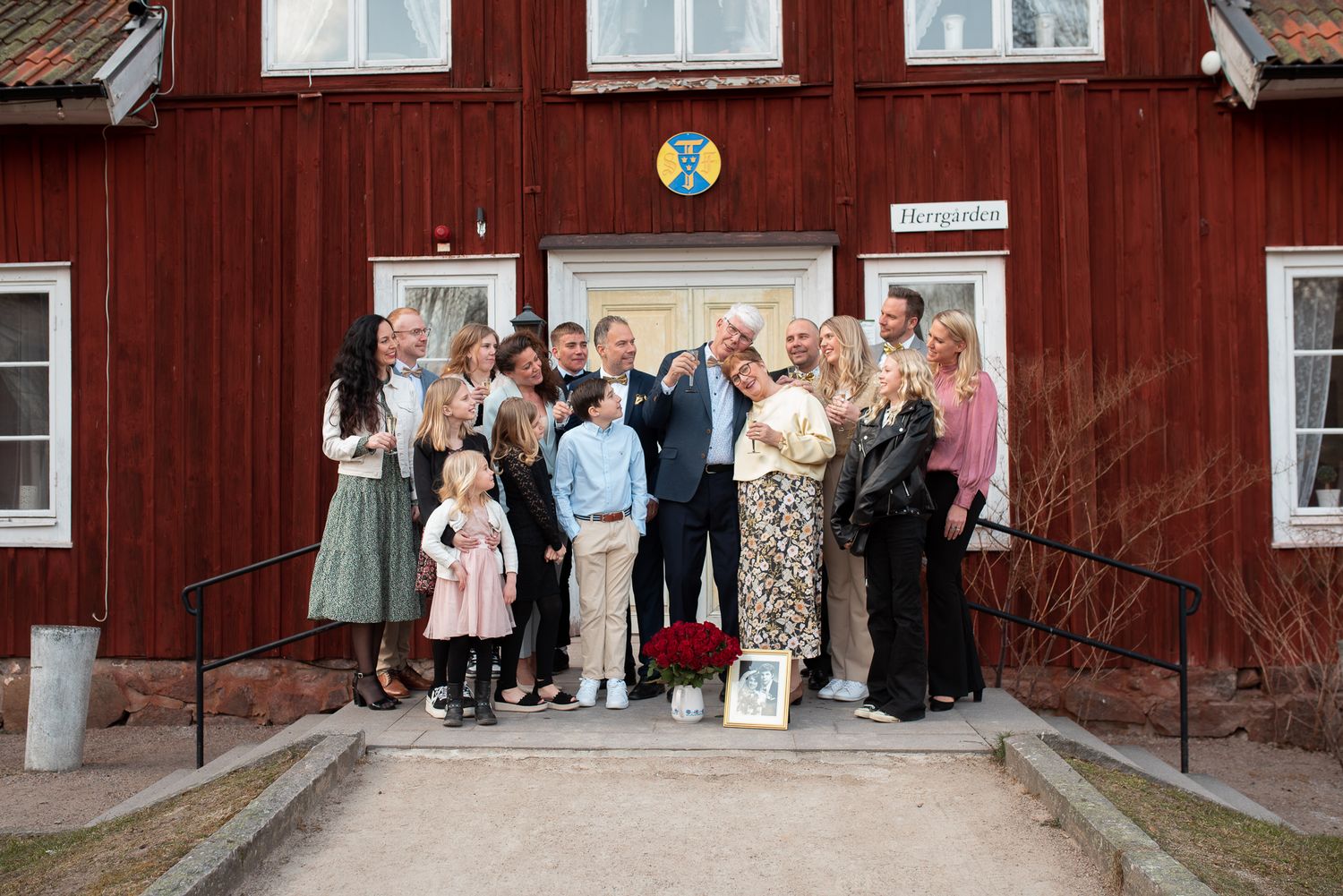 Large group gathered on stairs in front of traditional red Swedish building for celebration photo.
