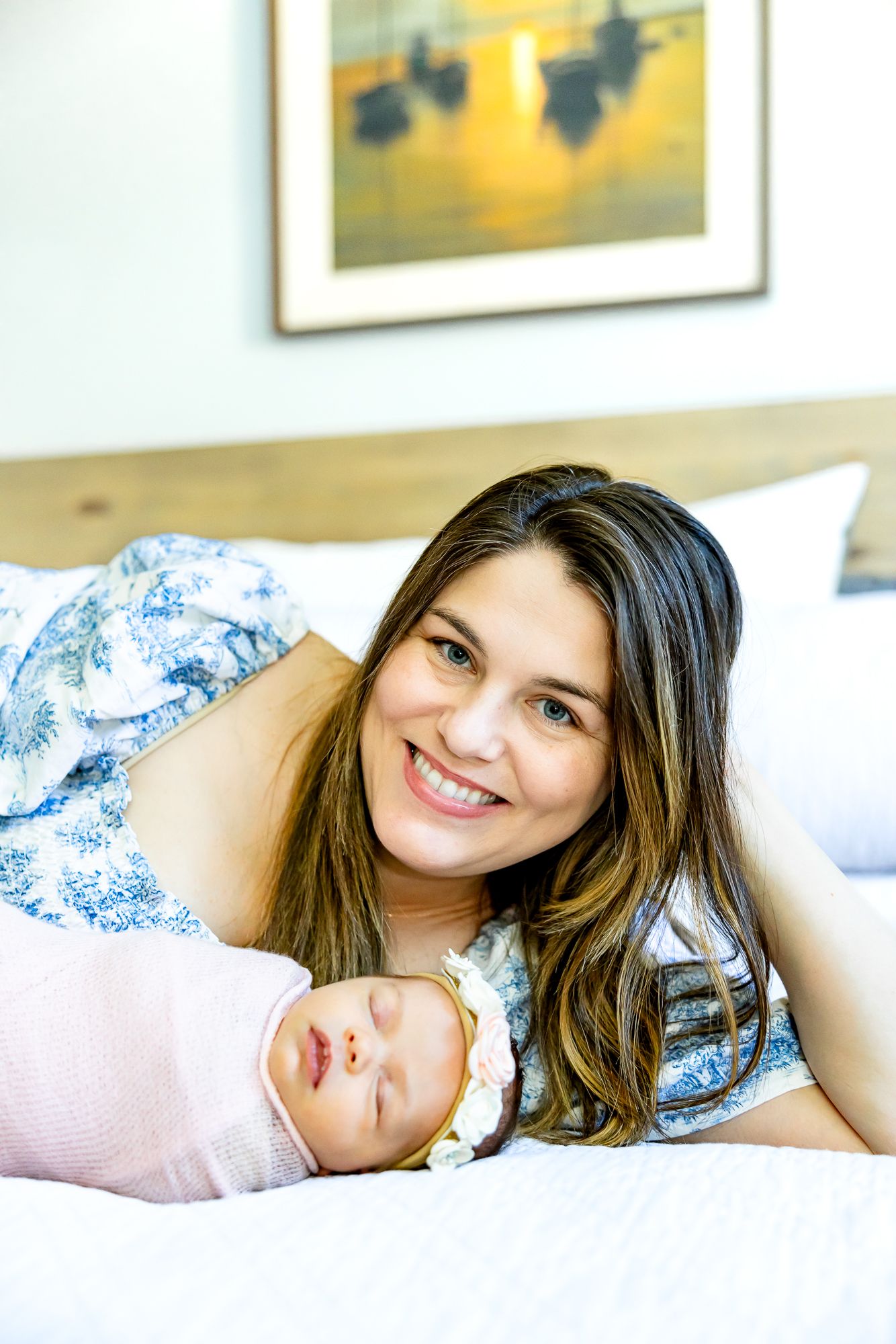 Mom lays on the bed smiling with her new baby girl next to her during lifestyle newborn photos in Colorado Springs.