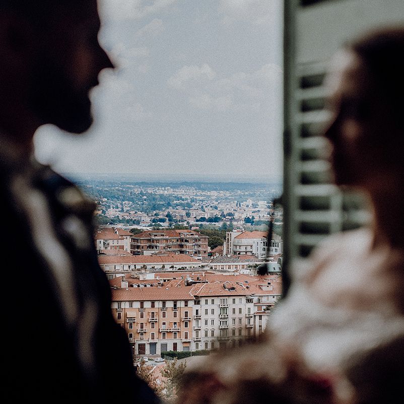 Couple silhouetted in a window frame with a stunning aerial city rooftop panorama visible behind them.