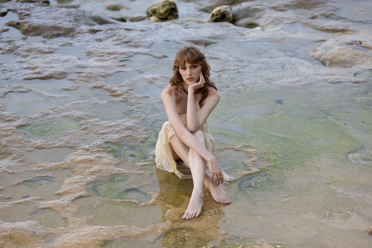 Person sitting on rocks by shallow water on a sunny day.
