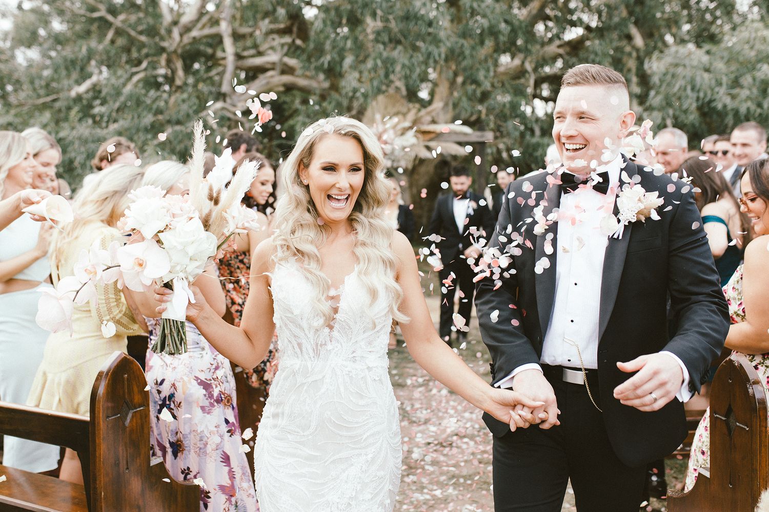 Wedding celebration with guests throwing petals and confetti in natural outdoor setting.