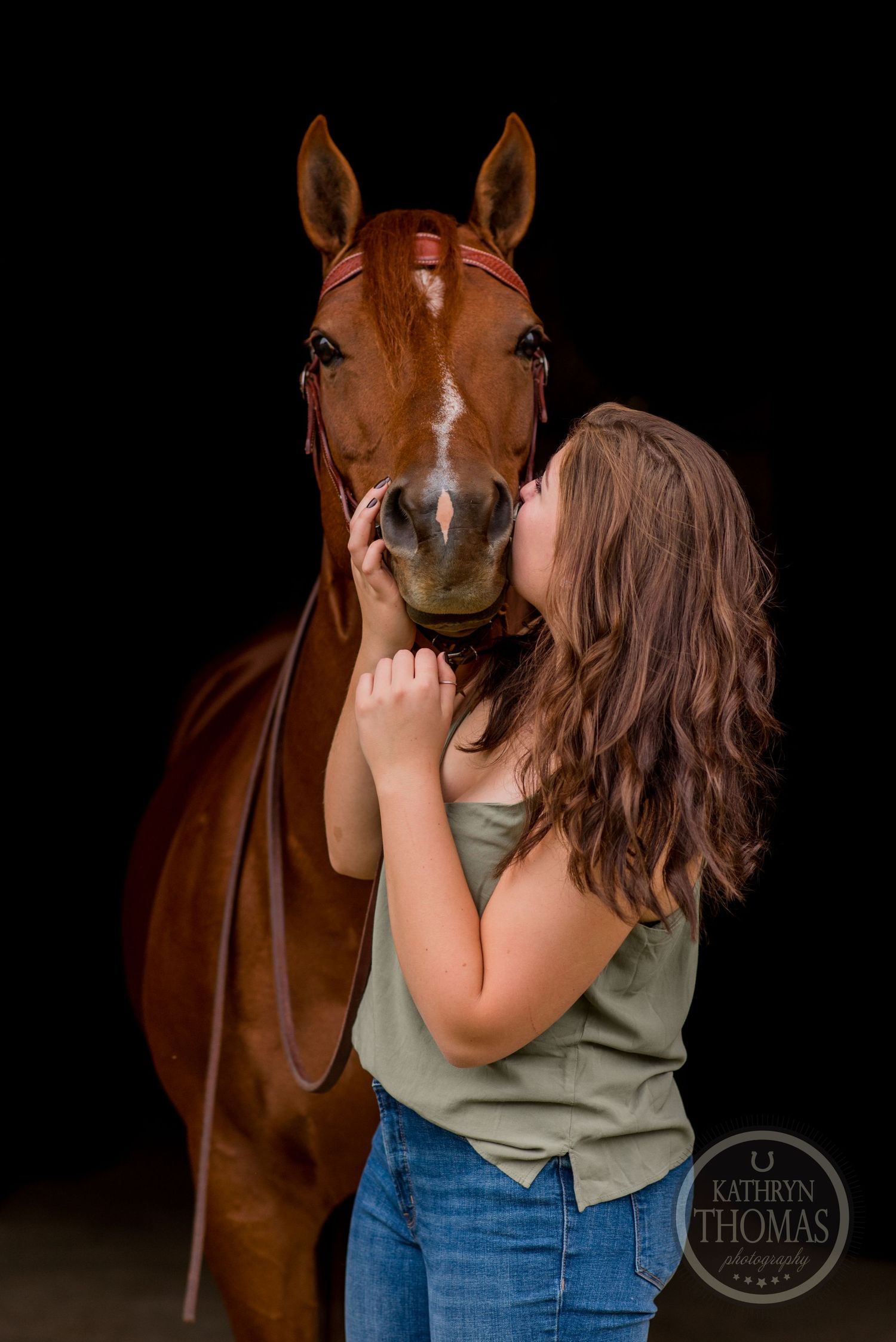 A tender moment between a chestnut horse and person in a dark studio setting.