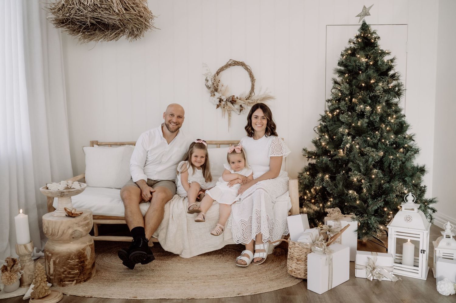 A series of festive minimalist family portraits with a white and neutral color scheme next to decorated Christmas trees.