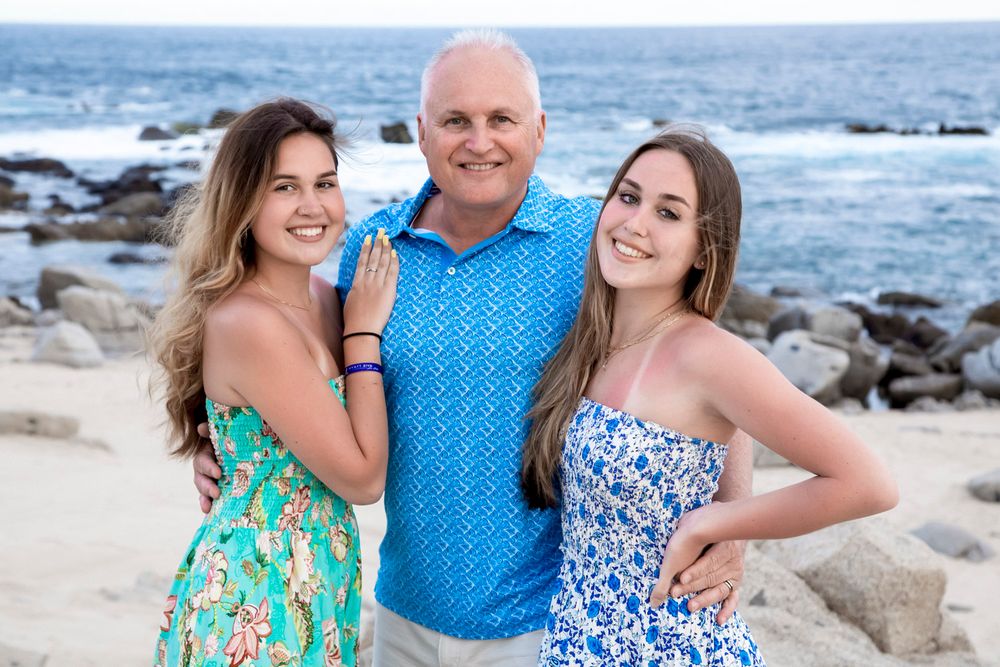 father and daughters on beach with ocean behind them