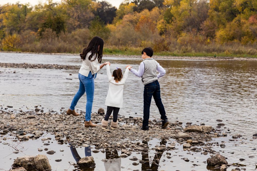 three kids holding hands on the river in warm clothing