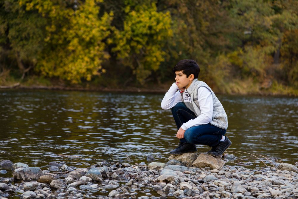 pre-teen kneeling down looking at the river in the autumn