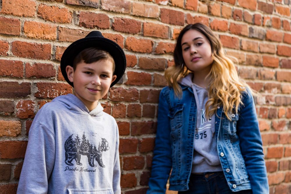 brother and sister leaning against a brick wall