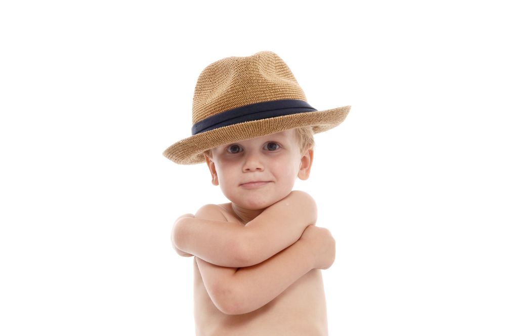 A confident toddler wearing a brown fedora hat against white background.