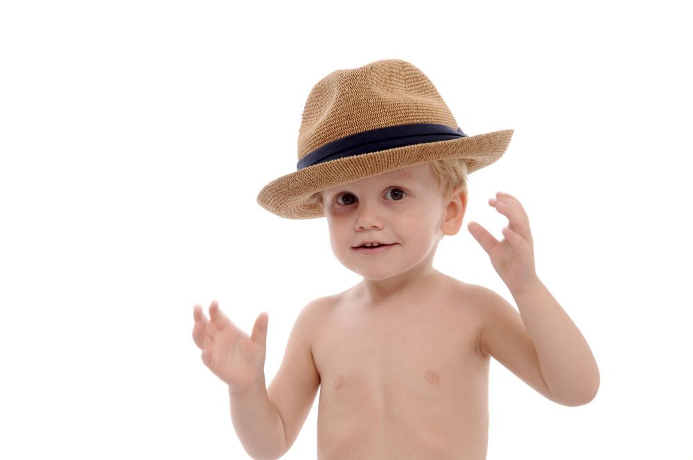Child in tan fedora hat gesturing with raised hands against white background.