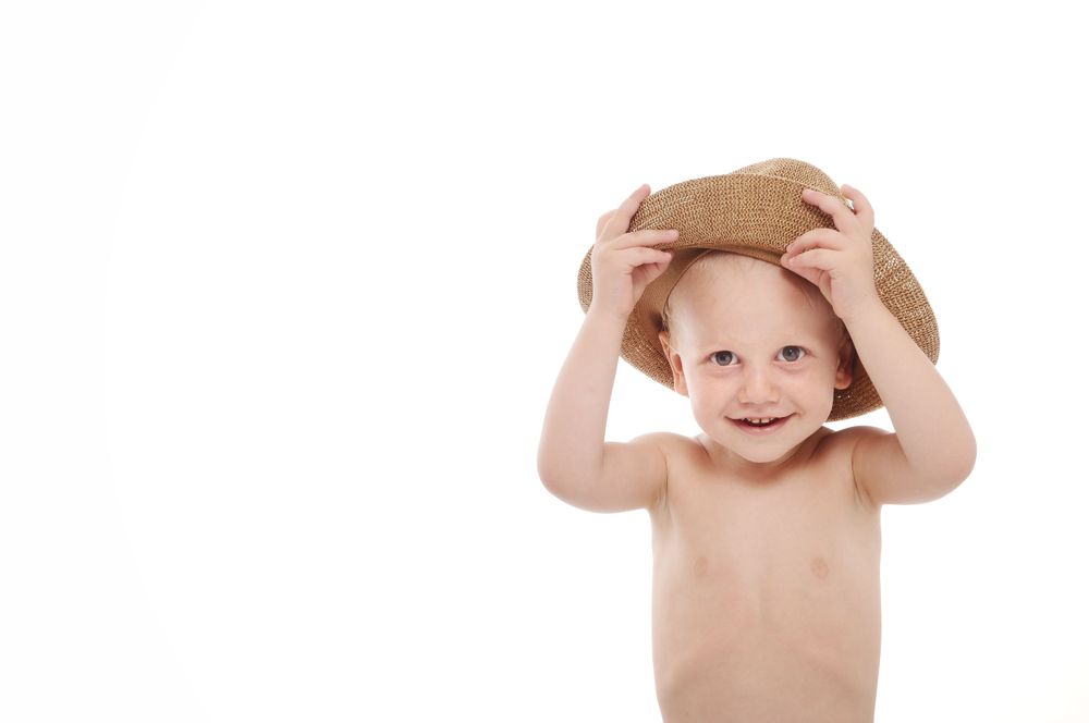 Child adjusting straw hat with both hands while smiling.