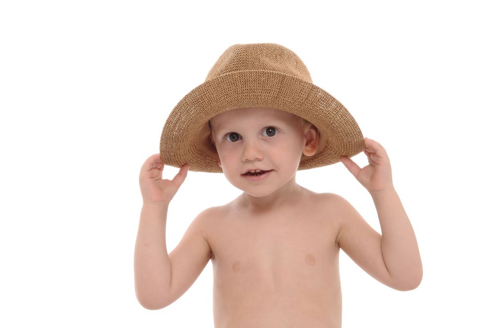 Child holding brim of tan sun hat with both hands against white background.