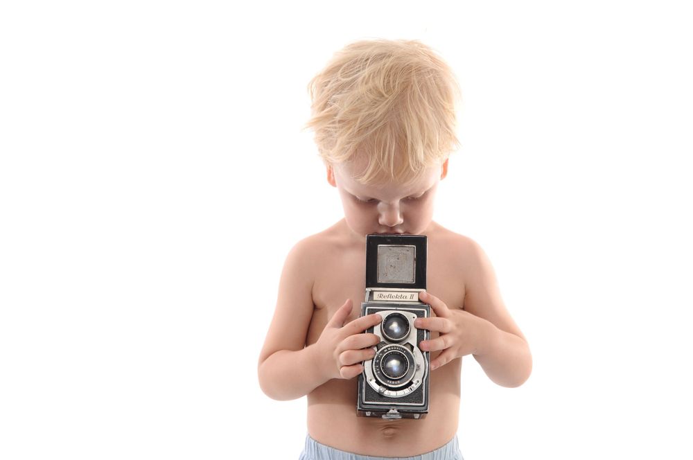 Child looking down at vintage camera held close to chest.