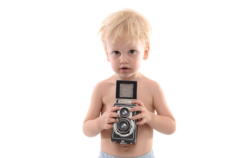 Child holding vintage twin-lens reflex camera against white background.