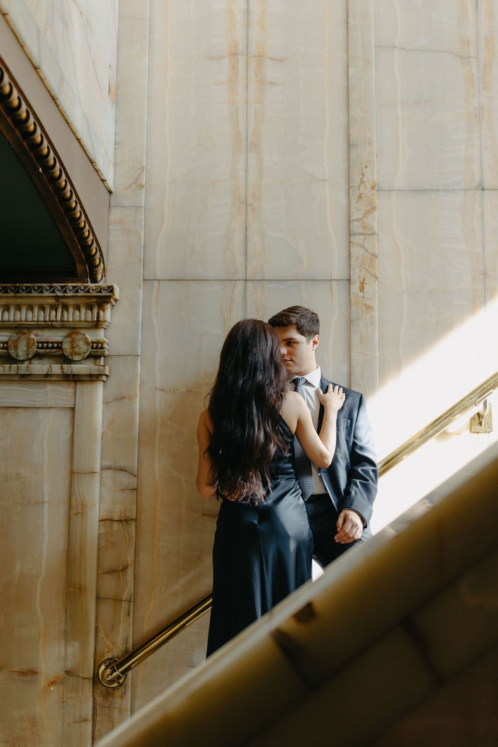 A couple sharing an intimate moment on a grand staircase with dramatic lighting.