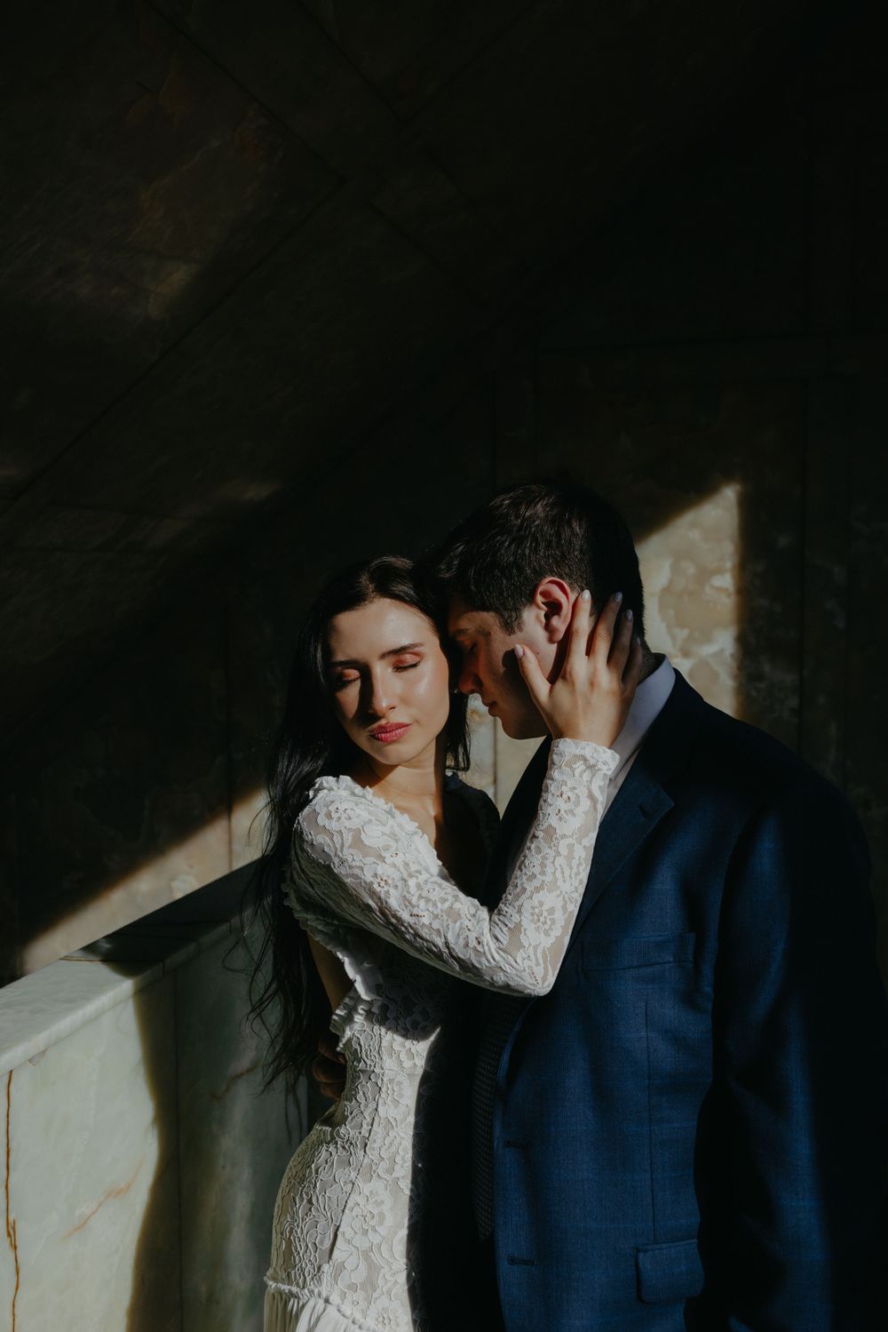 Dramatic portrait of couple in formal attire against dark wall with striking beam of light.