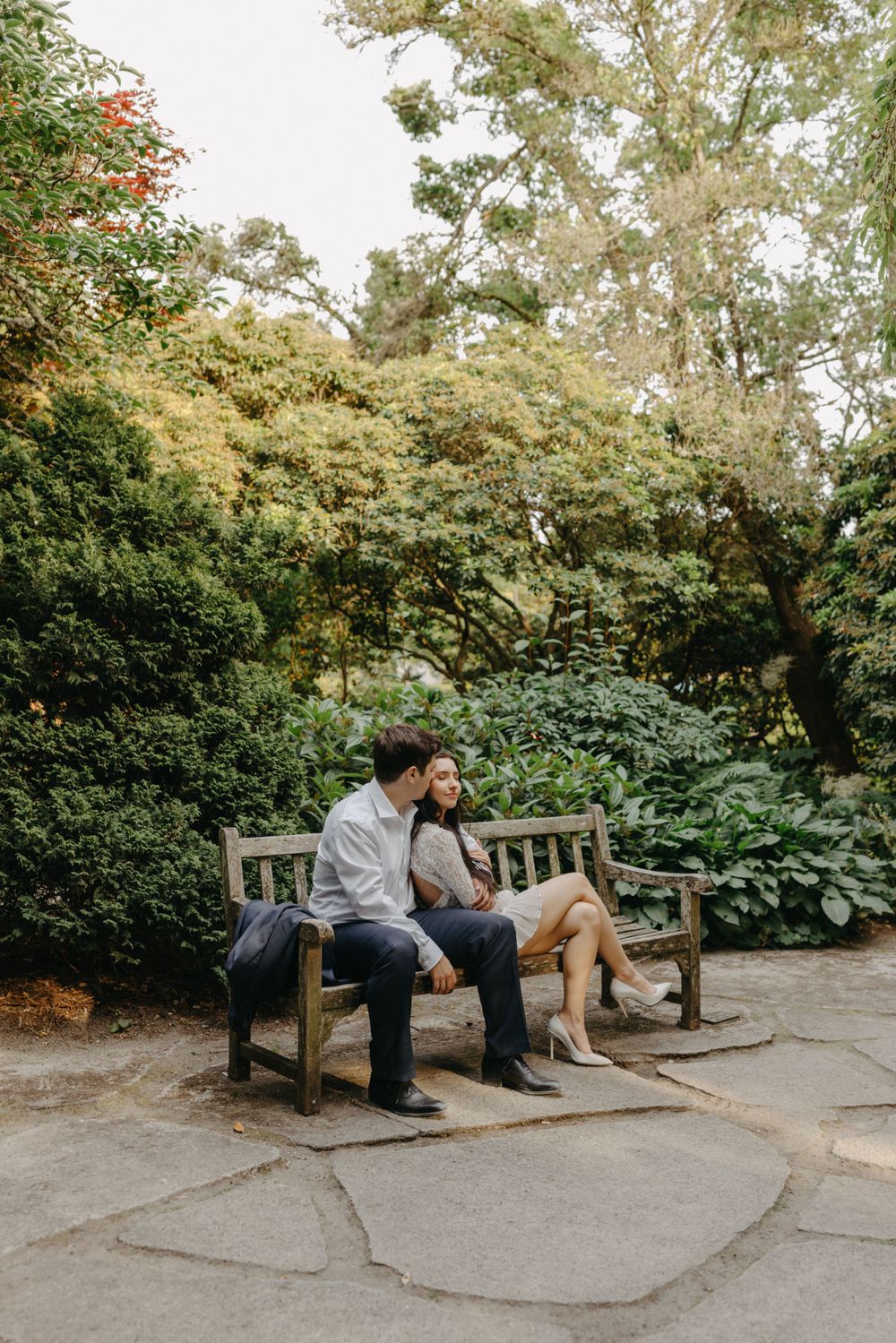 A couple sharing a quiet moment on a wooden bench in a peaceful garden setting.