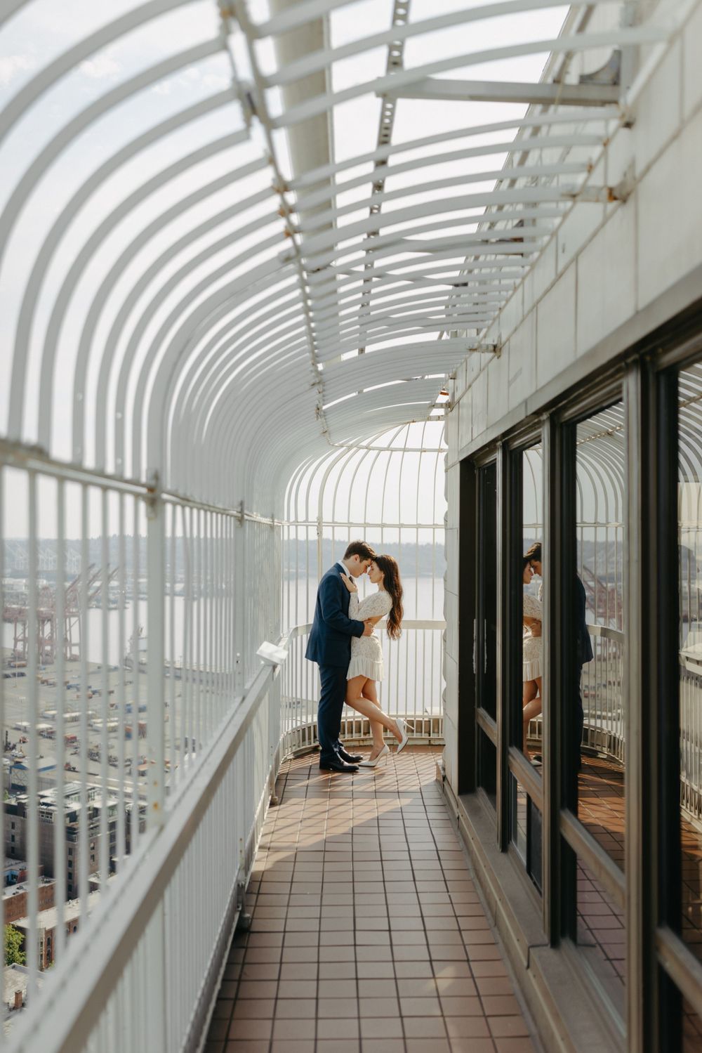 Elegant couple posed in curved architectural walkway with dramatic city views.