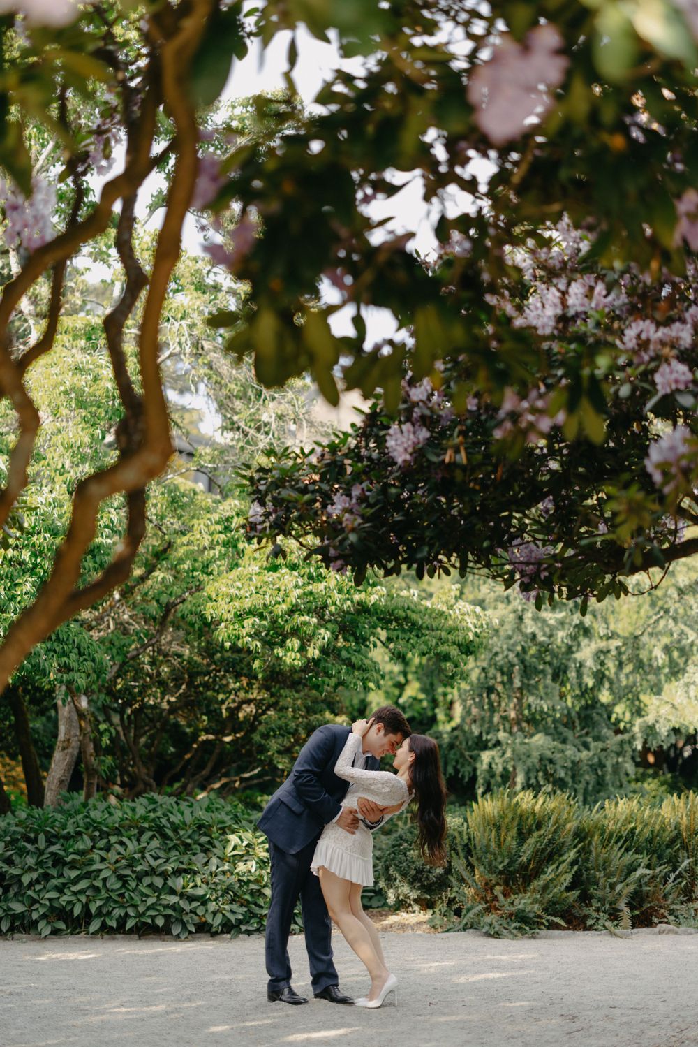 Couple sharing a romantic moment under blooming trees in a garden setting.