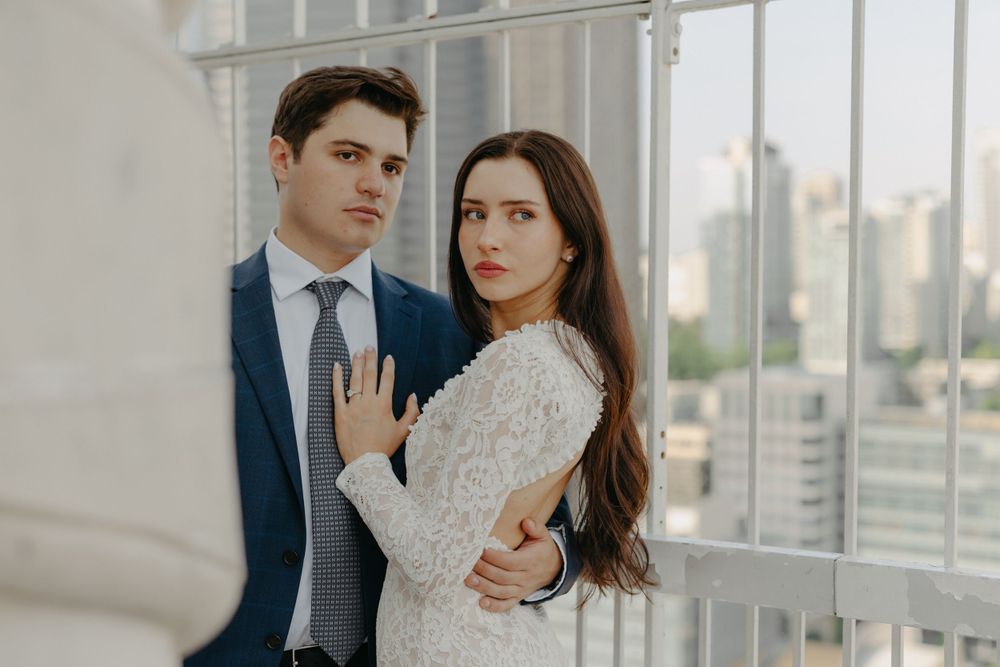 Elegant couple in formal wear posing together against a city backdrop.