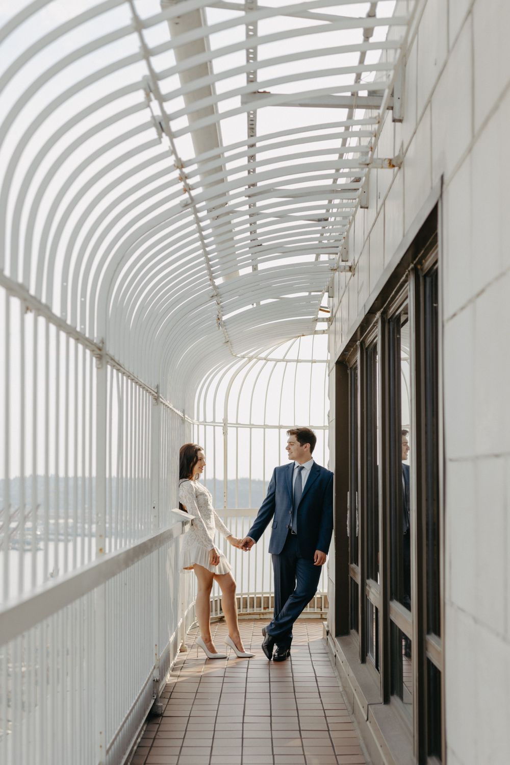 Couple holding hands in modern white curved corridor with geometric patterns and natural light.