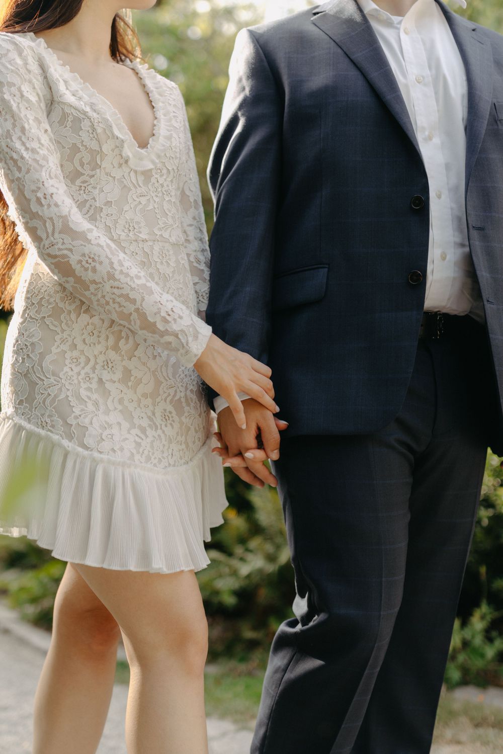 Close-up of clasped hands showing a white lace dress and navy suit details.