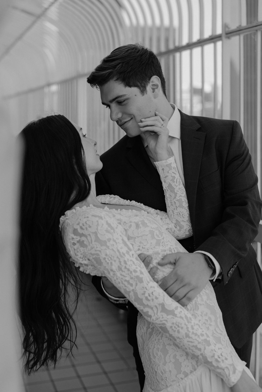 Romantic black and white portrait of a couple in formal attire embracing in a hallway.