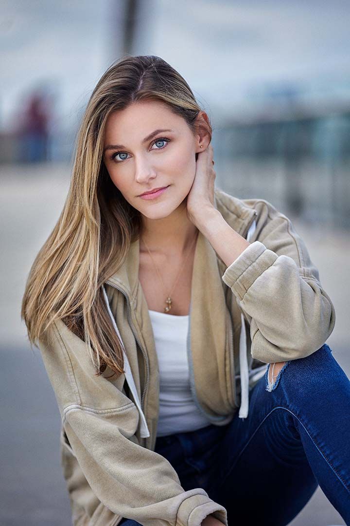 A fashion portrait of a person in a beige jacket and white top against a blurred background.