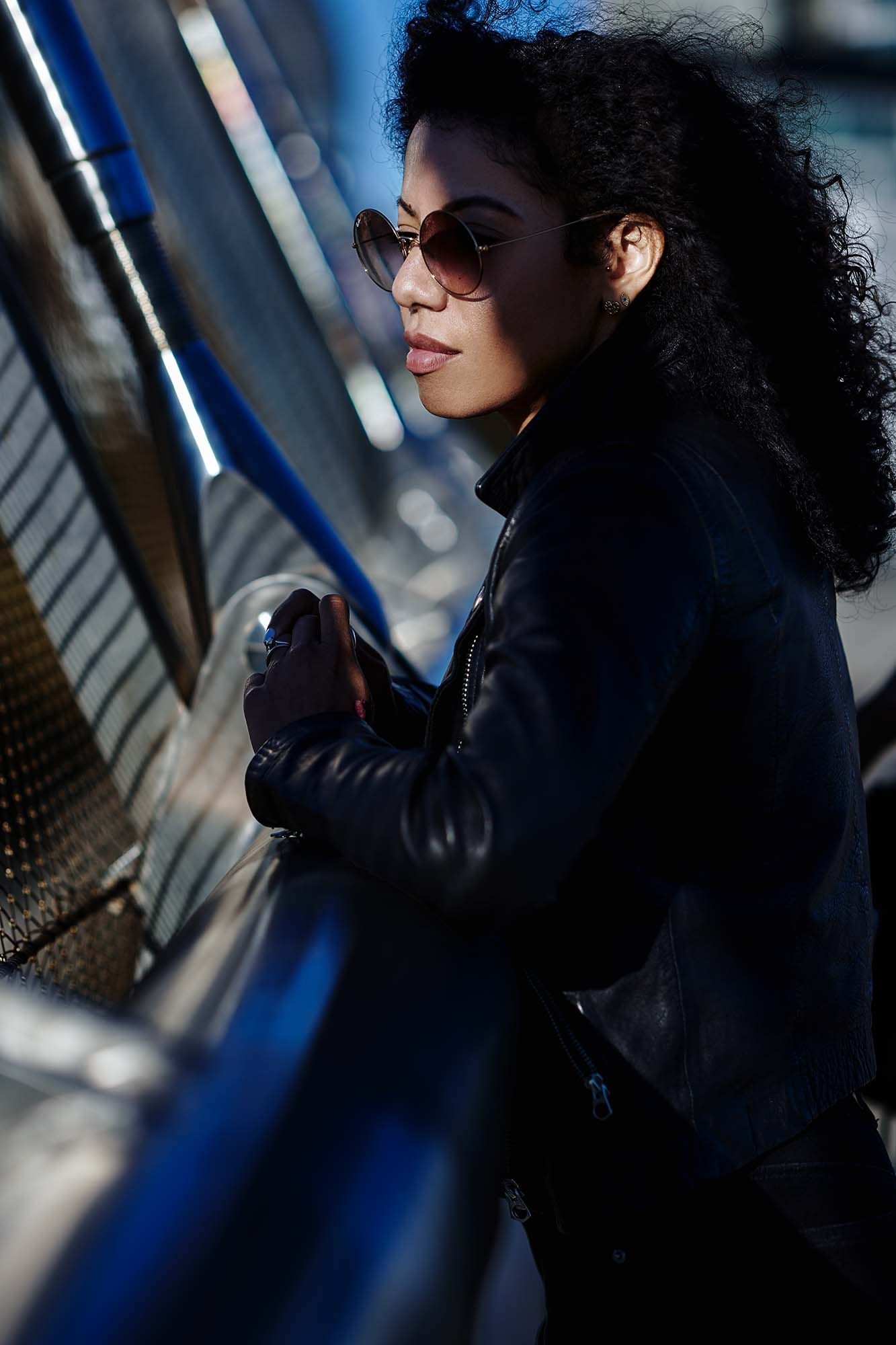 Candid portrait of a person with curly hair wearing sunglasses and leather jacket.