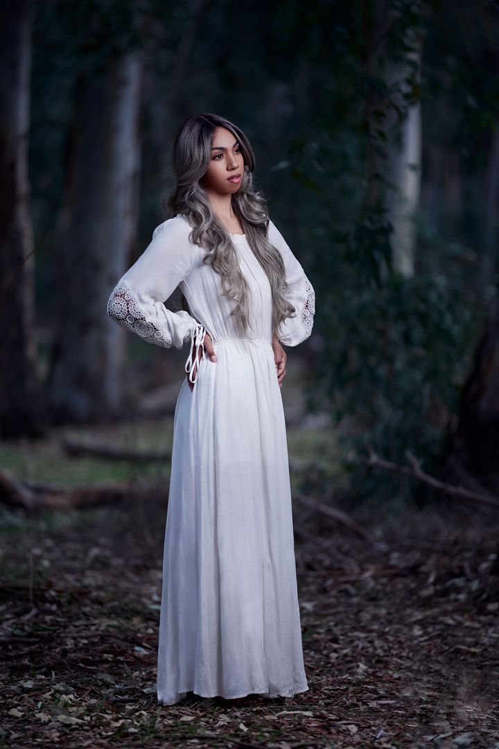A romantic white maxi dress with long sleeves photographed in a mystical forest setting.