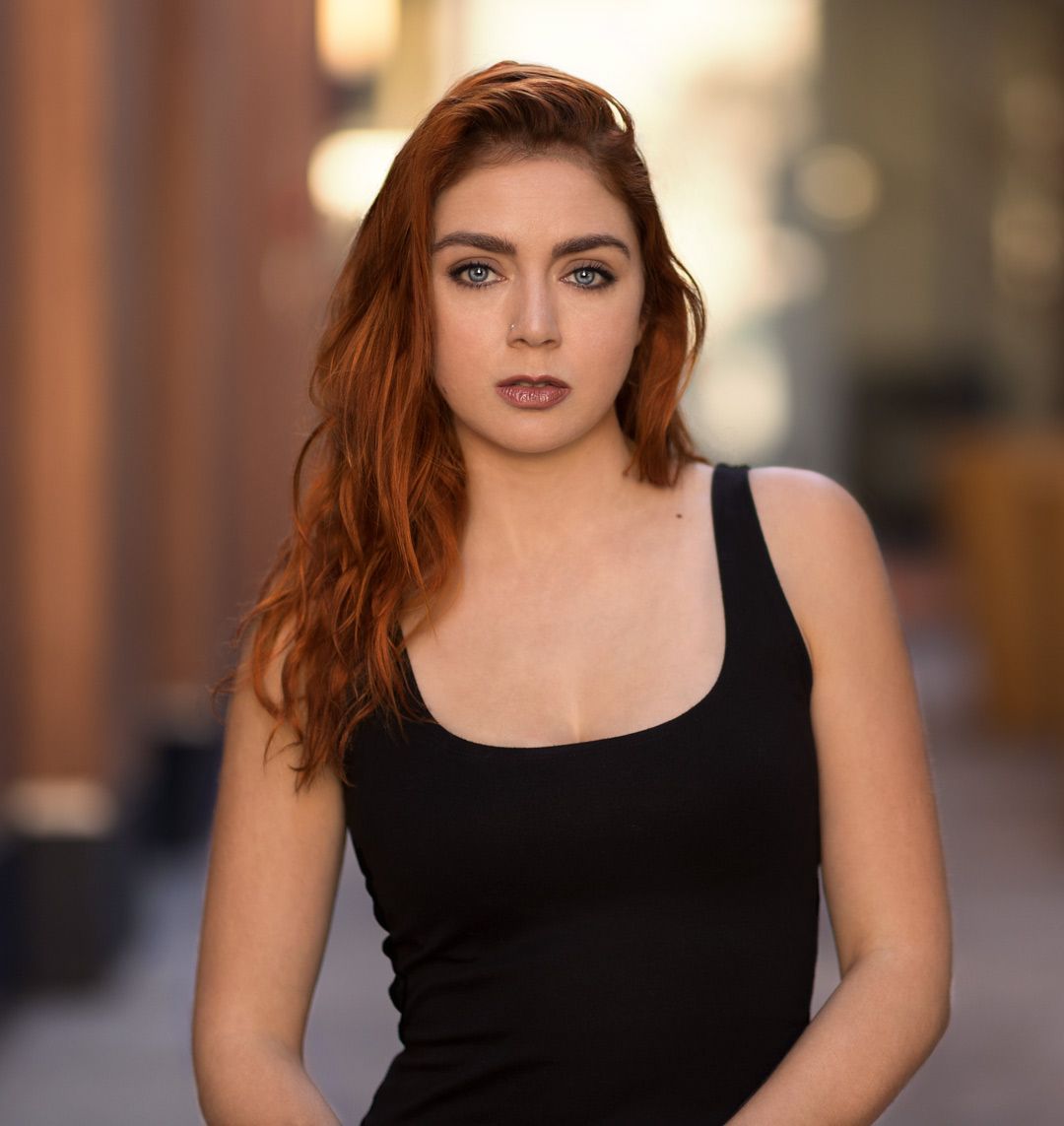 Portrait in black tank top with soft lighting and urban background.